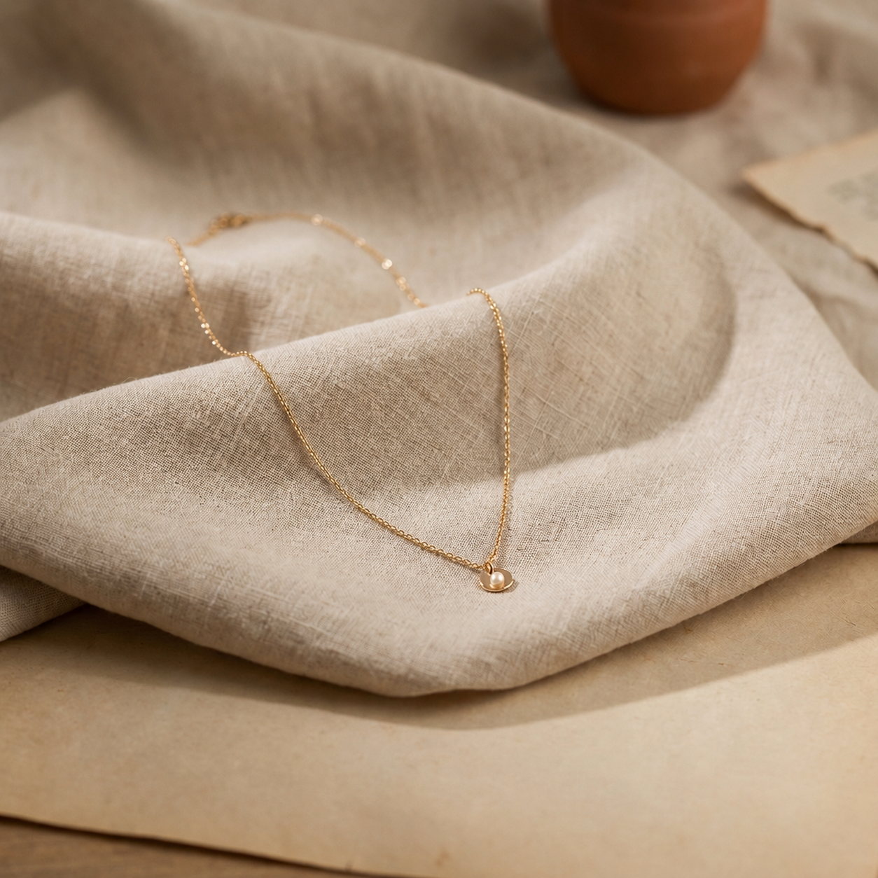 Fine gold chain necklace resting on draped natural linen